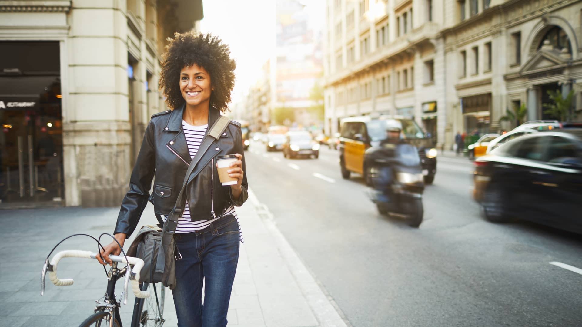 Mujer caminando sonriente y tranquila con su bicicleta mientras toma un café tras contratar un seguro de vida con la mutua