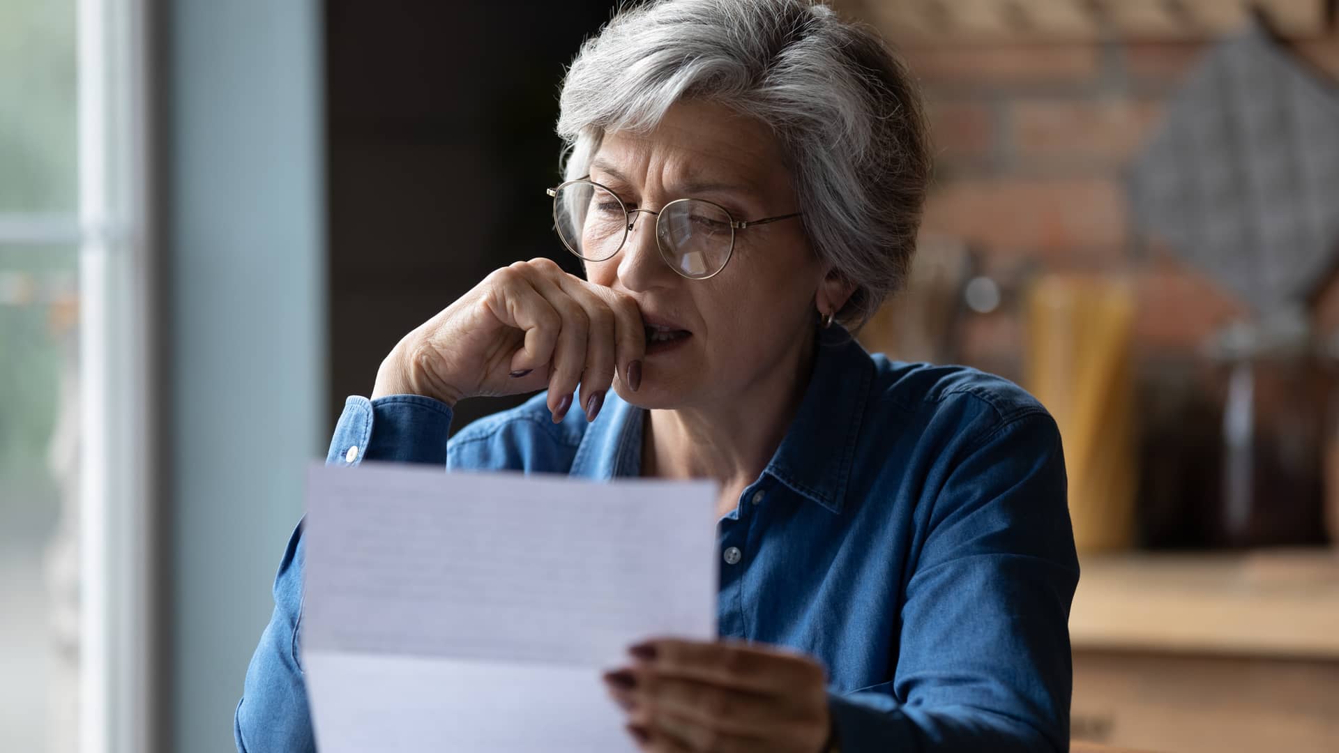 mujer de mediana edad leyendo una carta en la que aparece el reembolso de su seguro de asisa