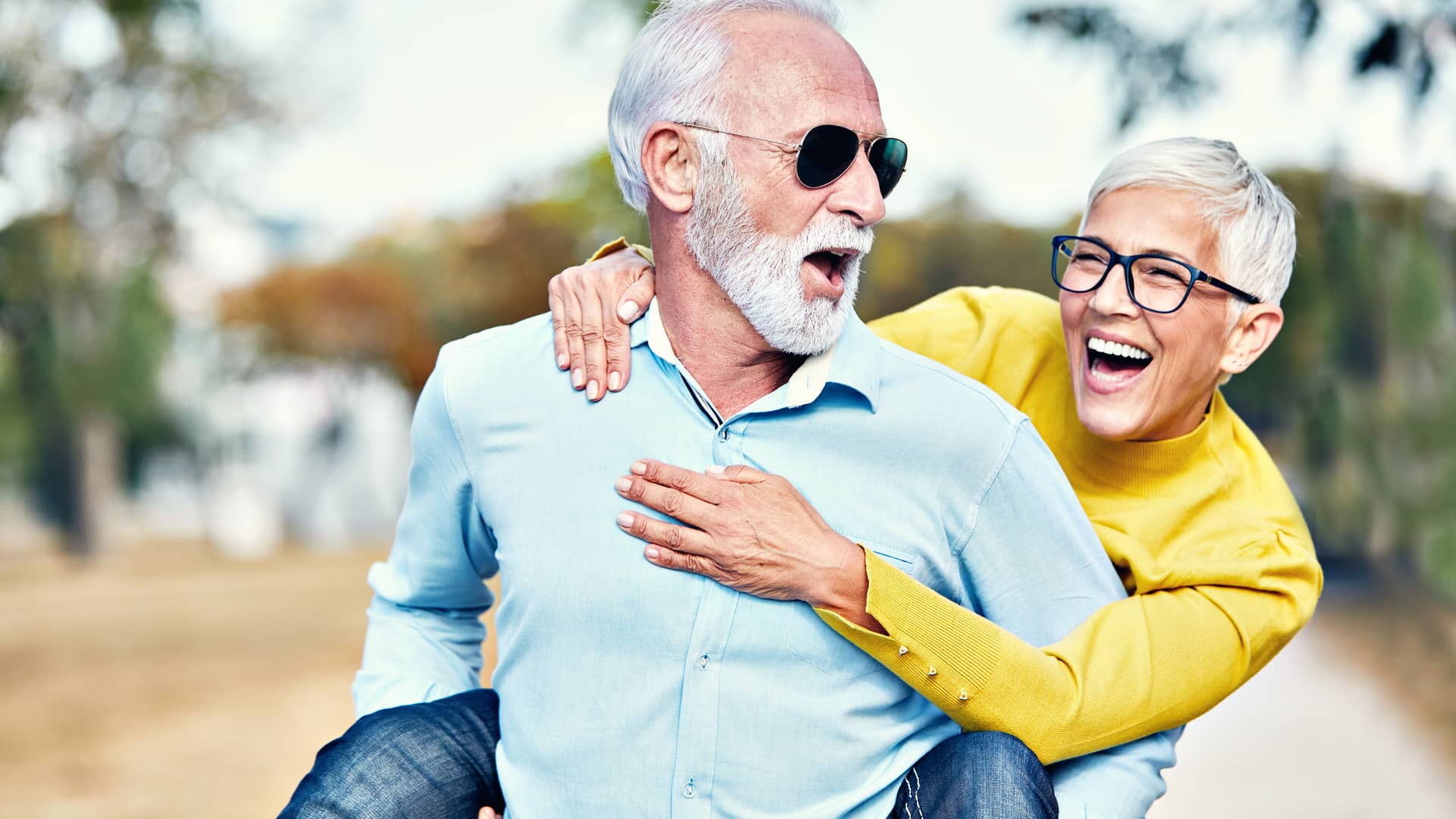 Una hombre de avanzada edad lleva a caballito a su mujer, ambos ríen tranquilos porque cuentan con un seguro Asisa sin copago