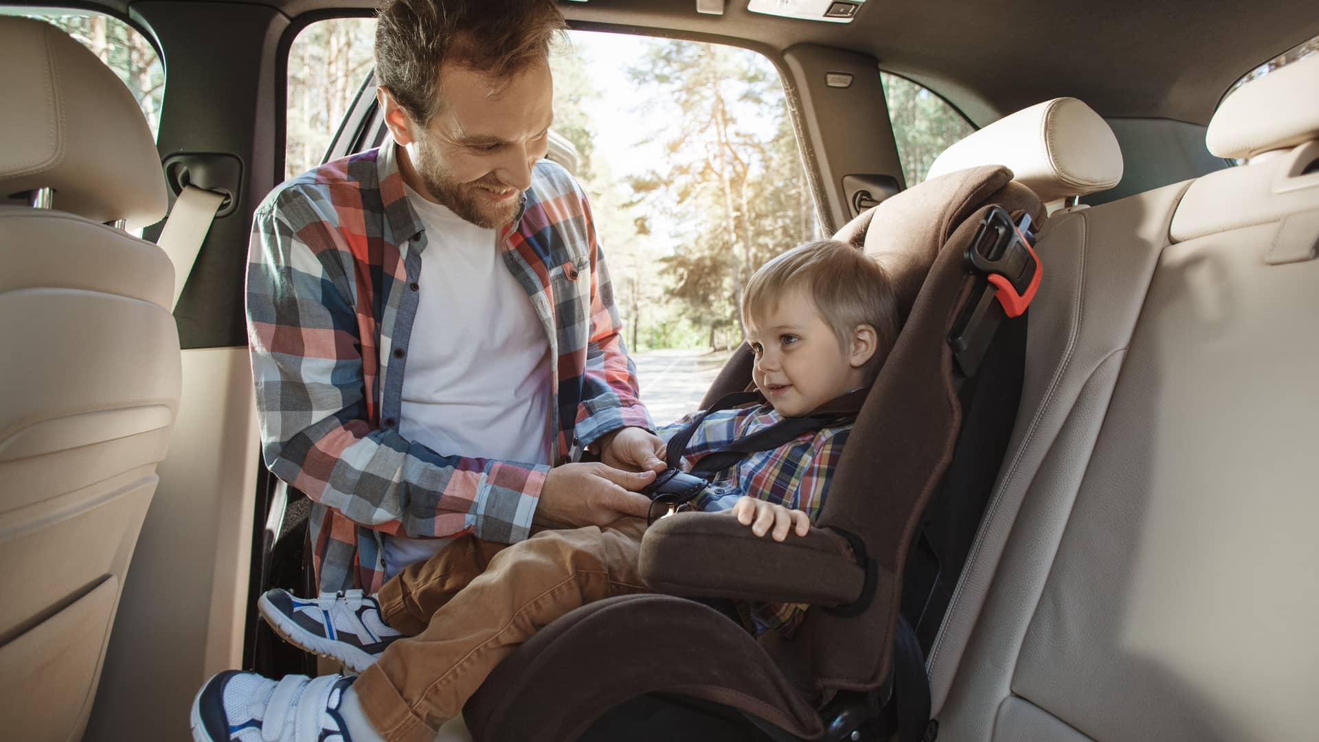 padre atando la silla de su hijo en los asientos traseros de un coche asegurado a todo riesgo con franquicia en mapfre
