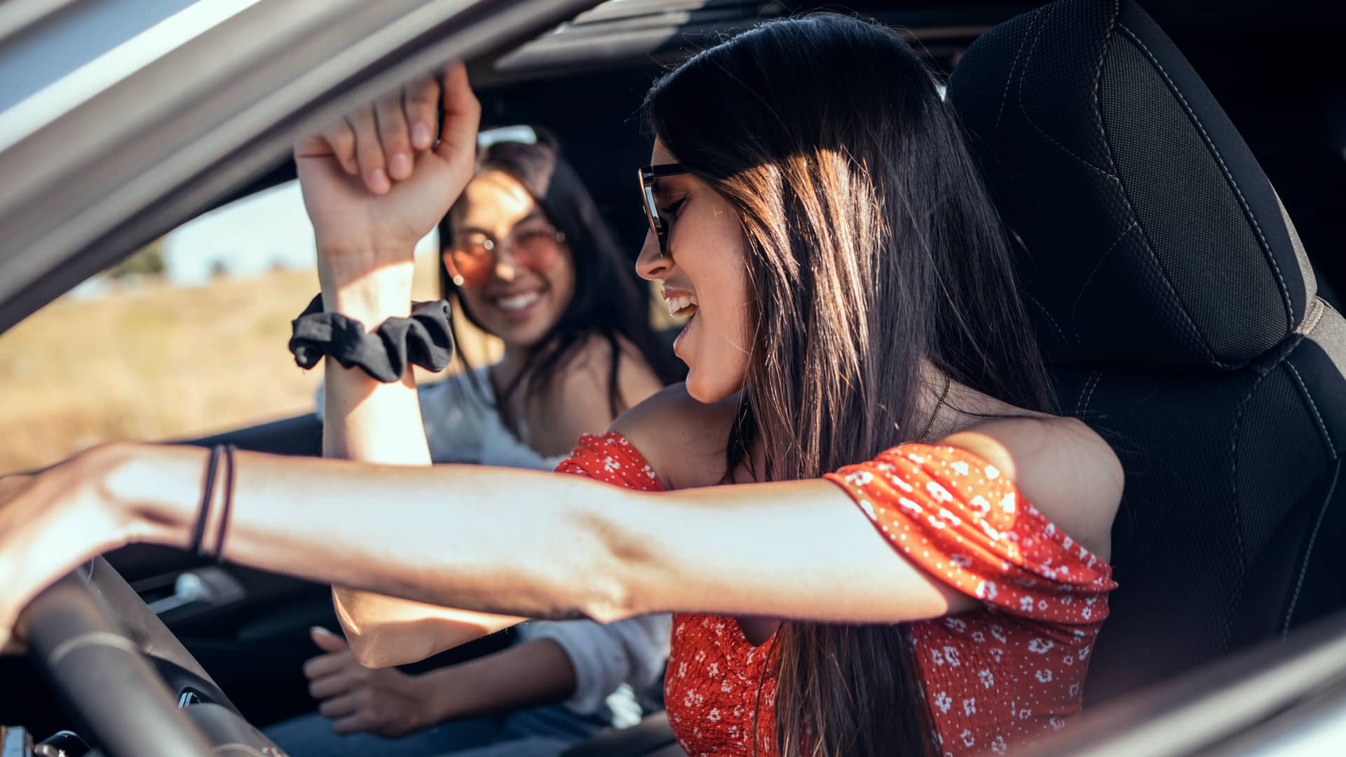 Mujer sonriente conduciendo su coche con seguro con compañía penelope junto a su amiga