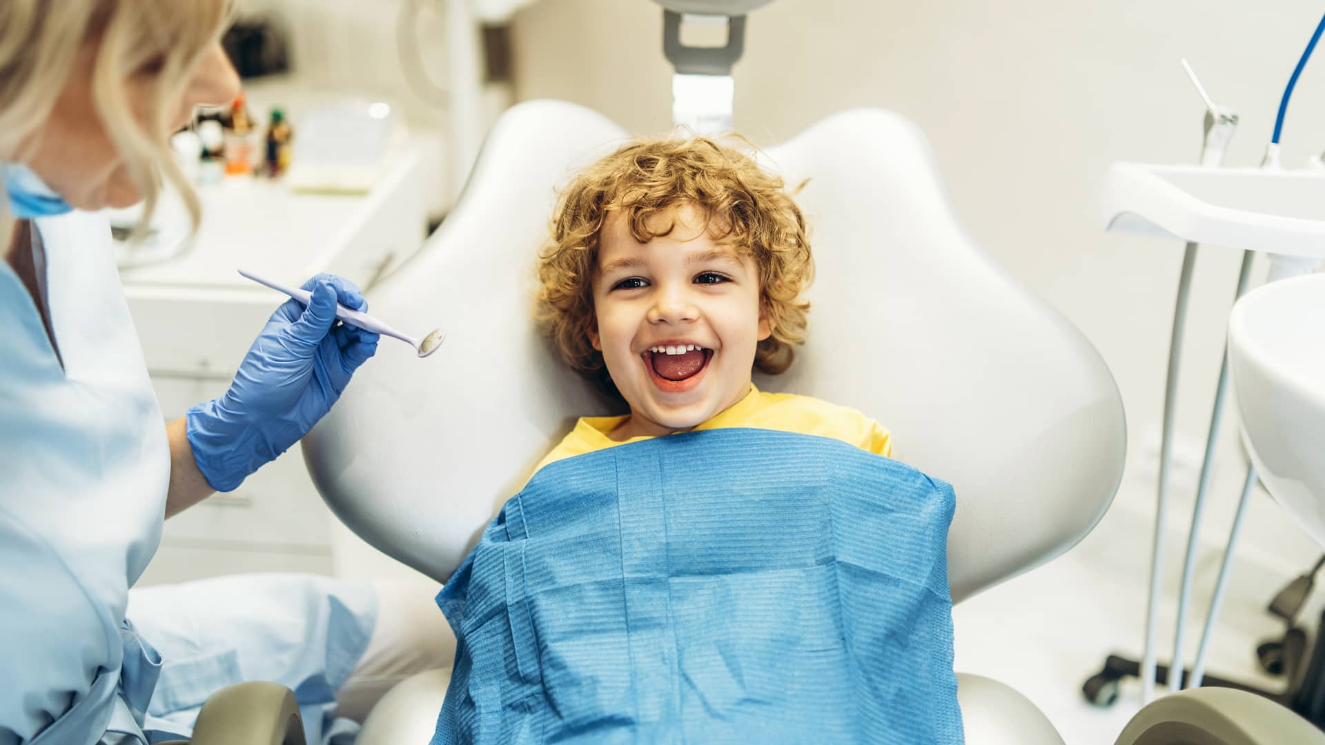 Niño pequeño de rizos sonriendo en la consulta del dentista porque tiene seguro dental premium de Sanitas