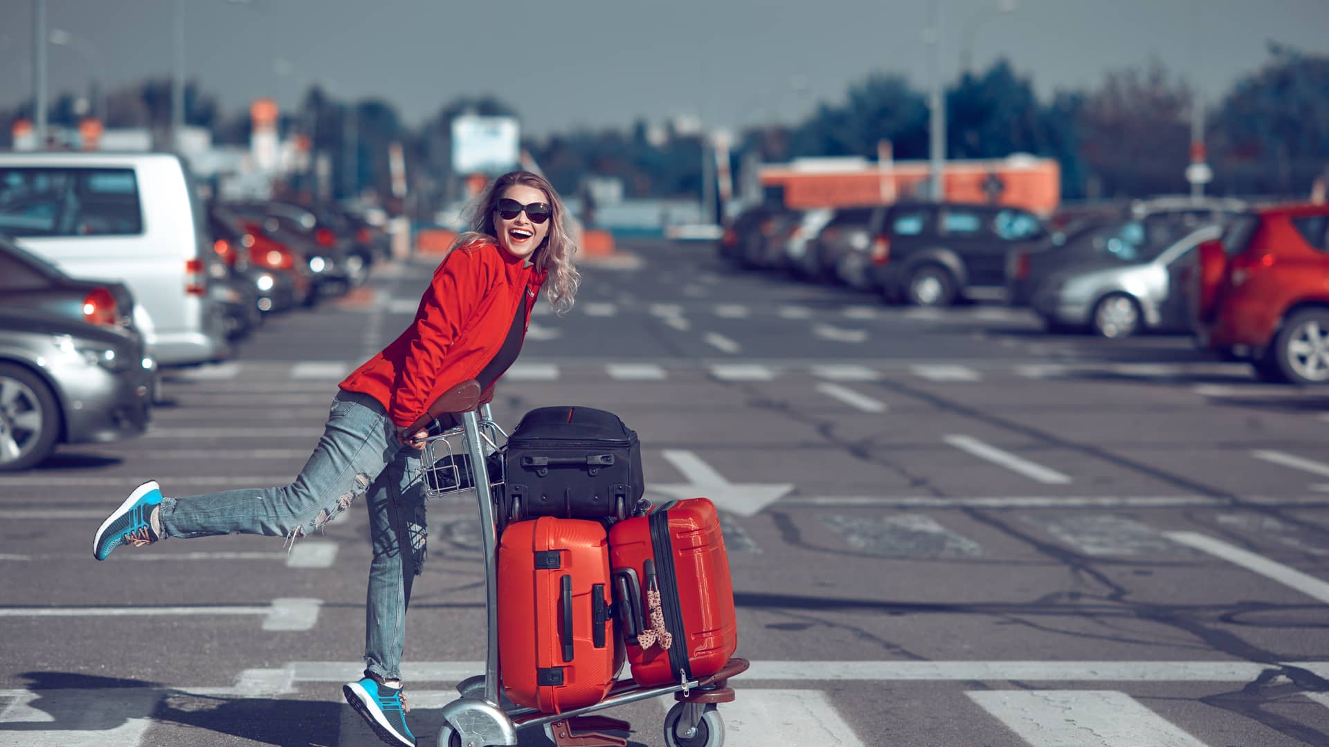 Mujer alegre empujando carro con maletas para irse de vacaciones para tomar su vuelo con la tranquilidad que le da saber que tiene un seguro de viaje con zurich