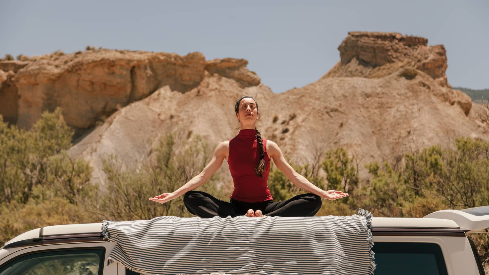 Mujer practicando yoga en el techo de una furgoneta en el desierto tras conseguir dar de baja seguro