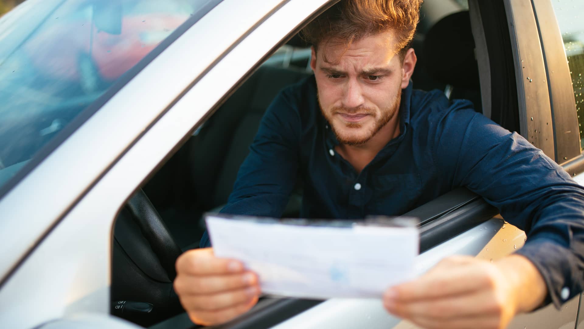 Hombre sentado en su coche leyendo la multa que acaba de recibir