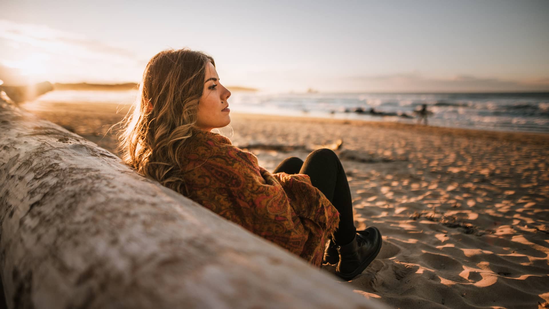 Mujer sentada en la playa frente al atardecer pensando que es lo que le cubre su seguro de decesos