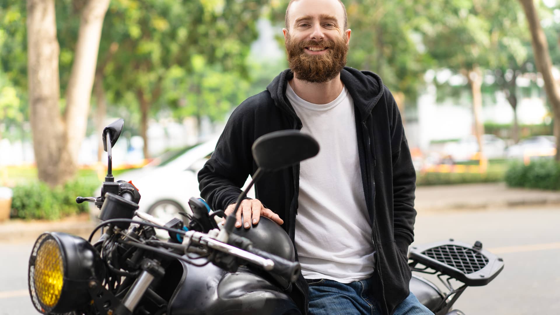 Joven sonriente sentado en su motocicleta de 150 cc con seguro contratado