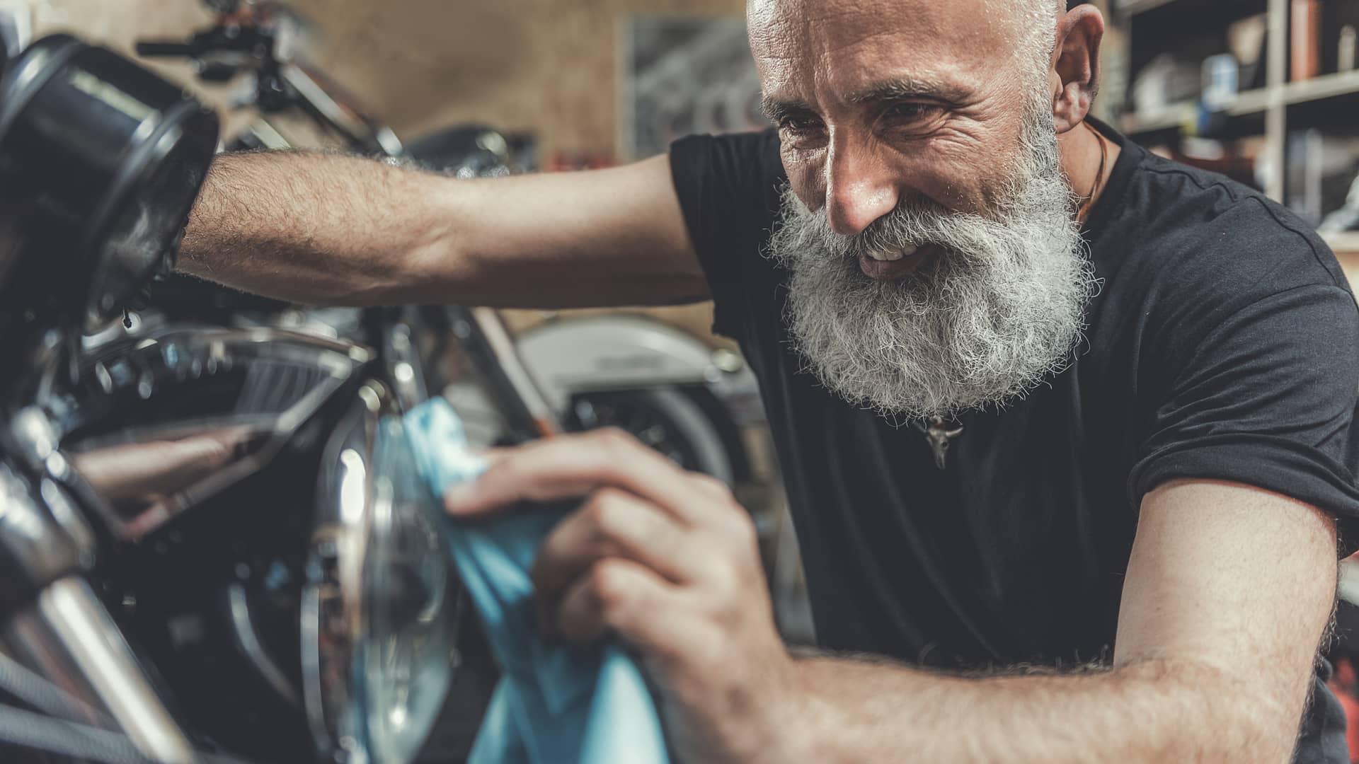 Hombre feliz limpiando su moto con seguro a todo riesgo concienzudamente 