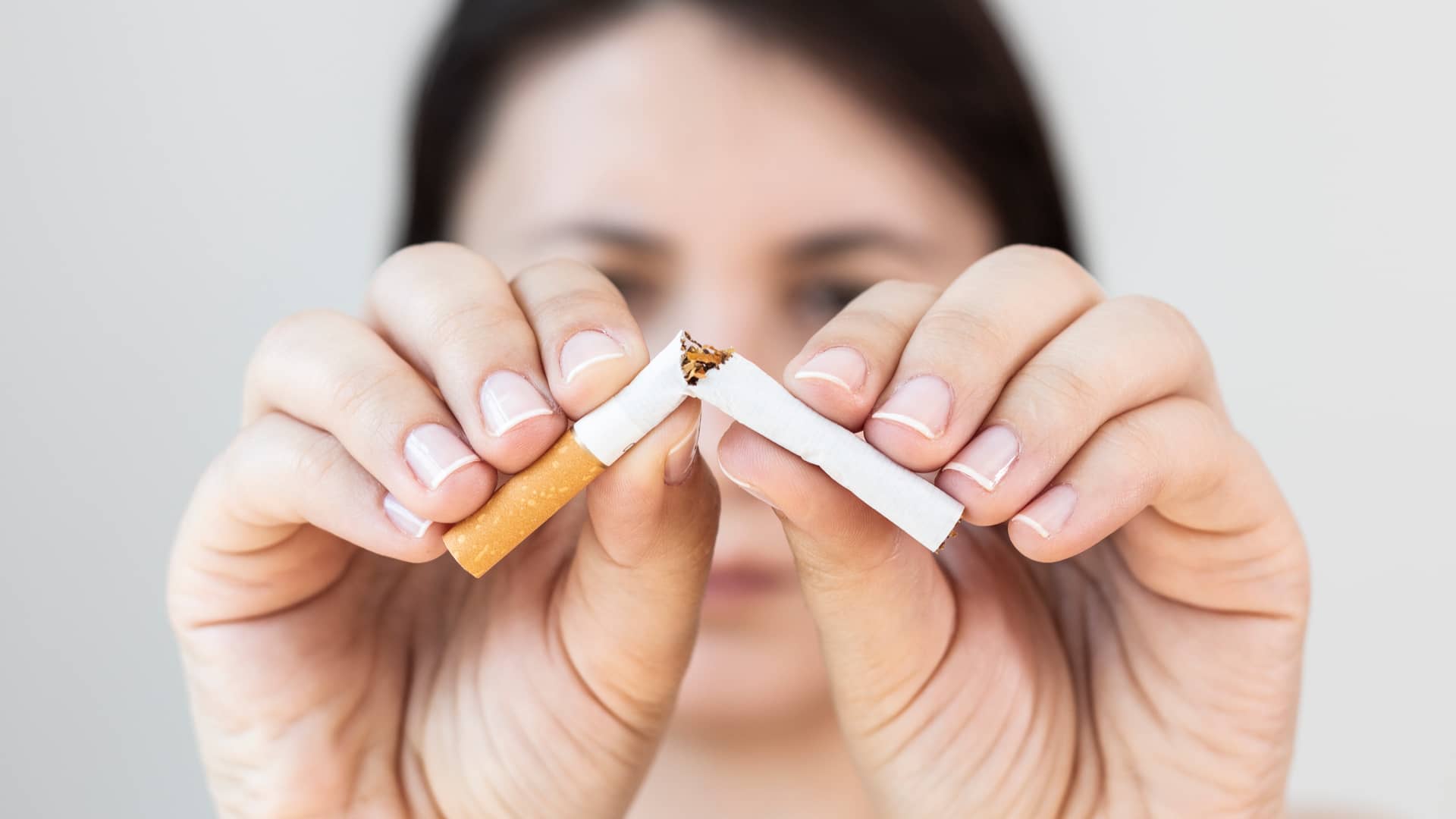 Mujer partiendo un cigarro a la mitad porque quiere dejar de fumar según recomendaciones de su médico de seguro de salud
