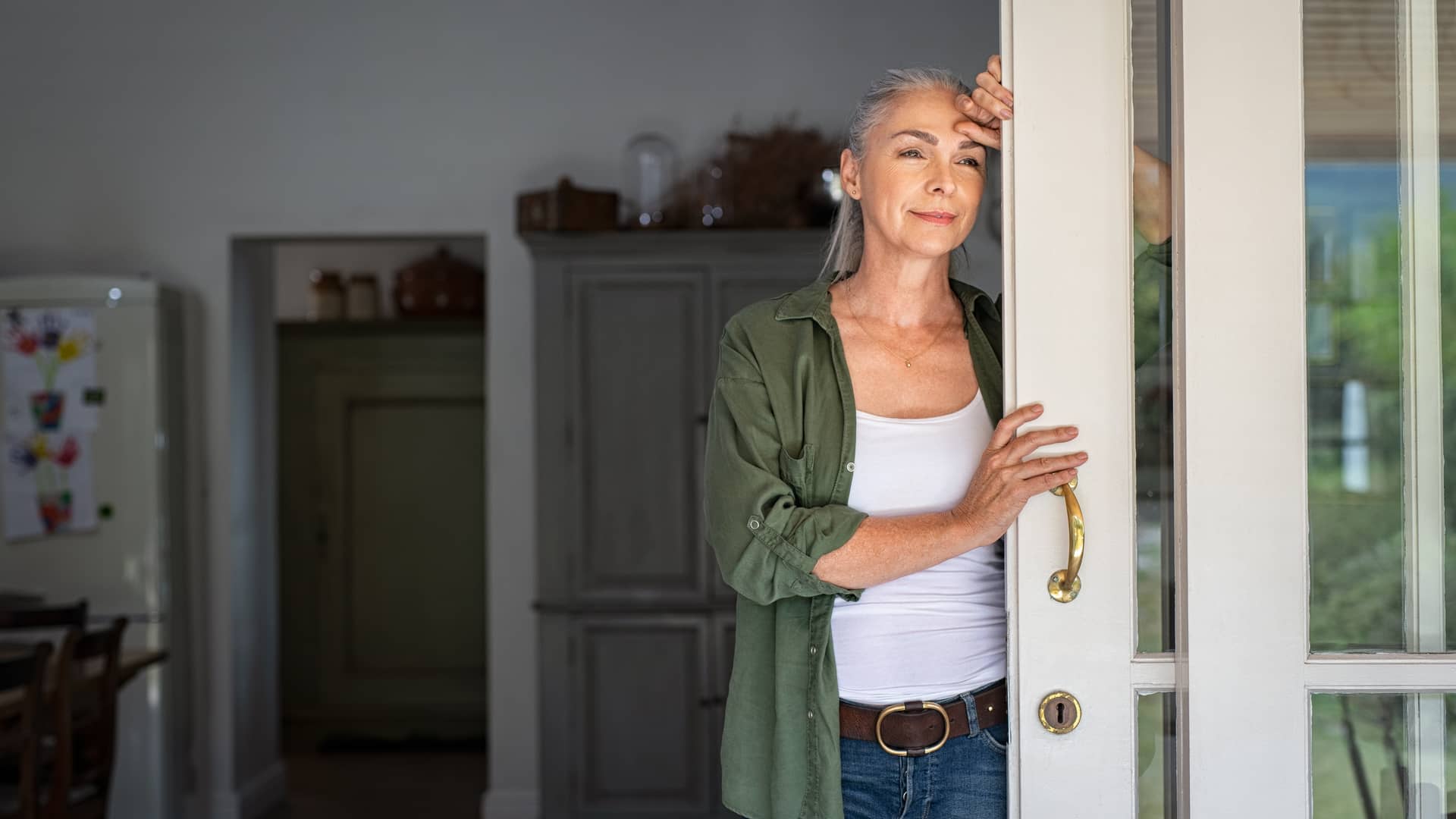 Mujer jubilada parada a la puerta de su casa pensando en las alternativas a su seguro de salud