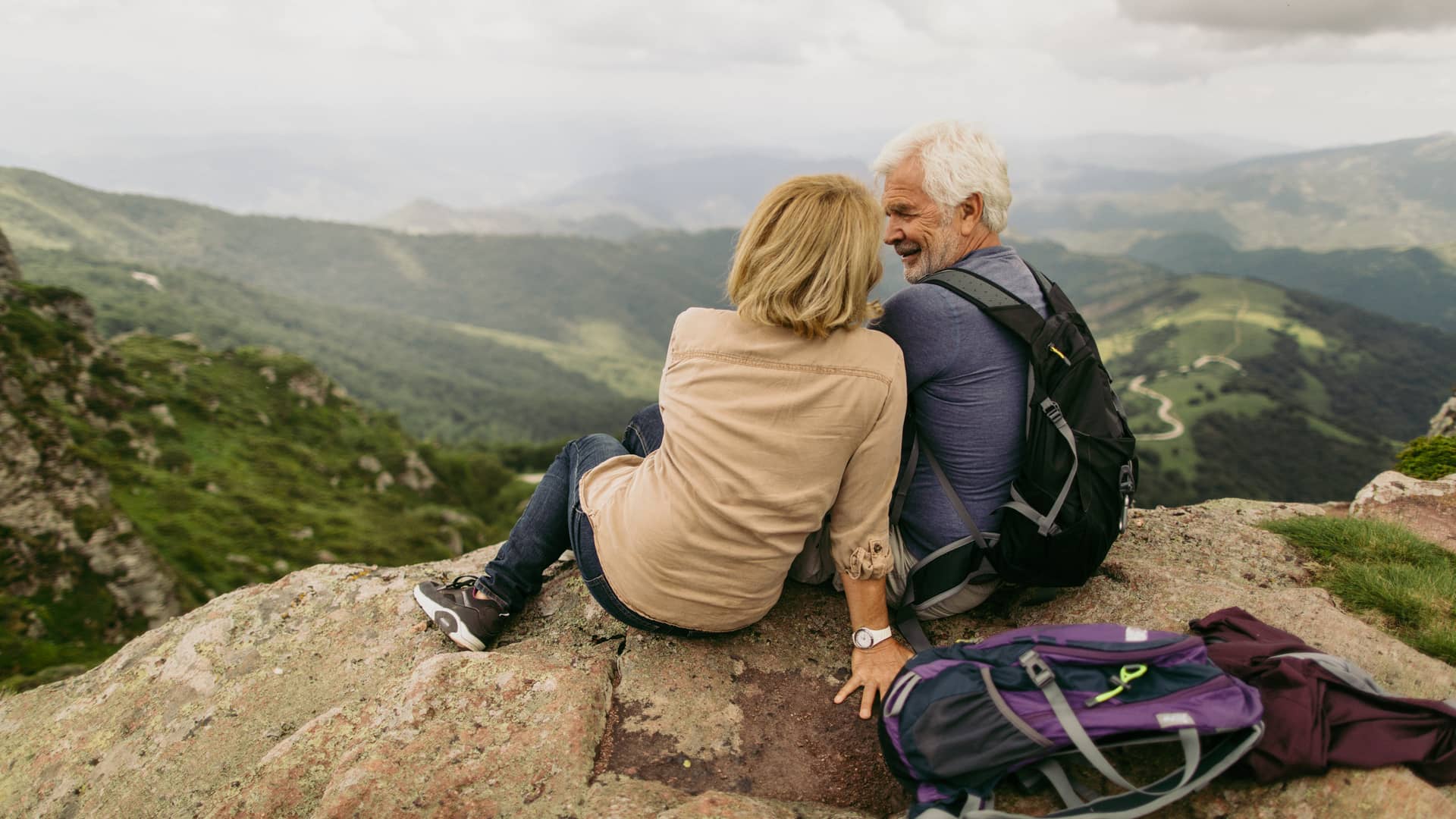 Pareja de la tercera edad disfrutando de las vistas desde arriba de la montaña y con la seguridad que les da tener un seguro de viaje para mayores